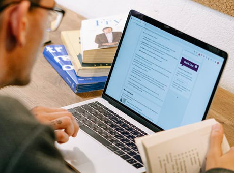A person studies using a laptop surrounded by books.
