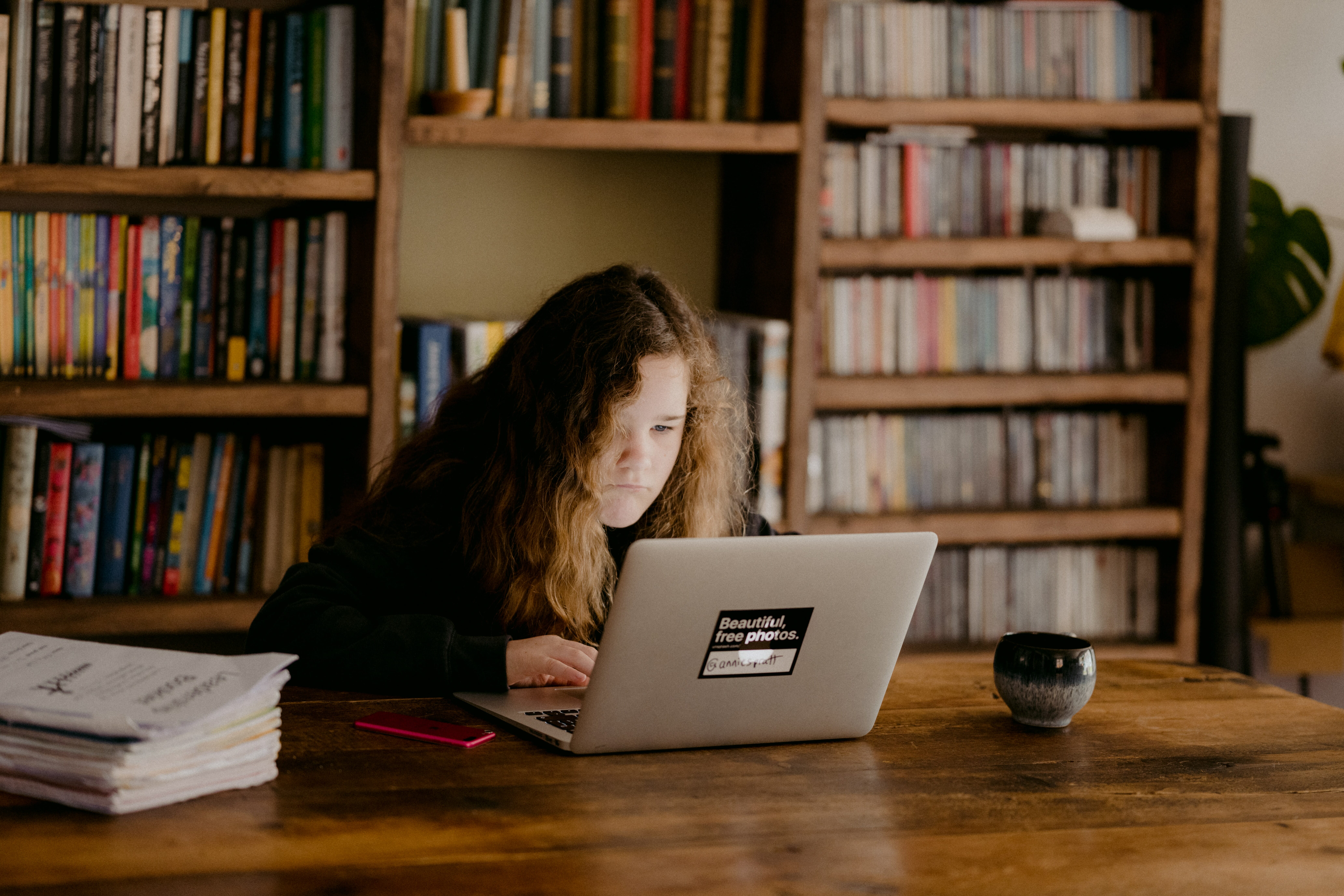 Teenage student studies on a laptop at a table in the library.