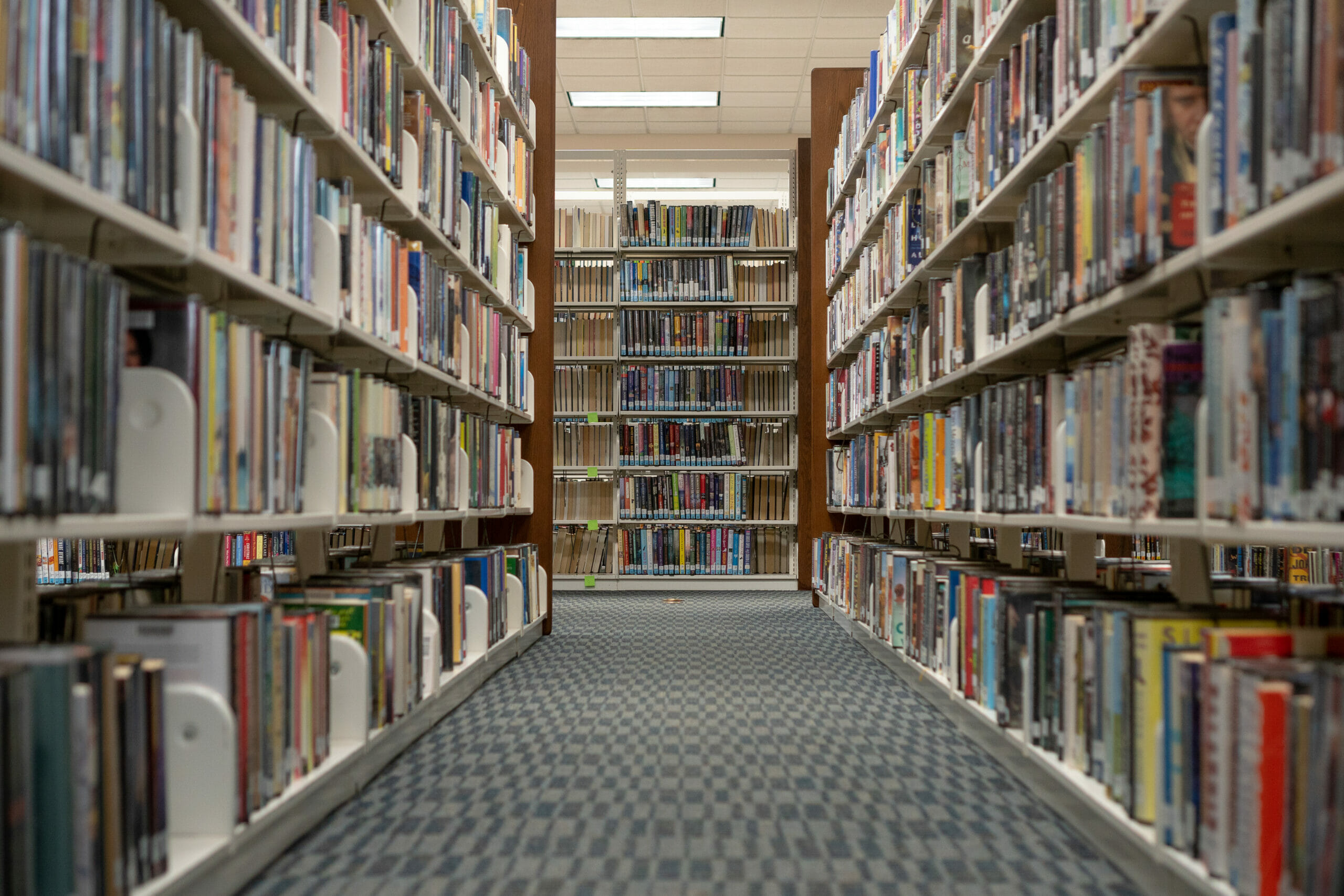 The view of an aisle of books, 6 shelves tall, full of books in the library.