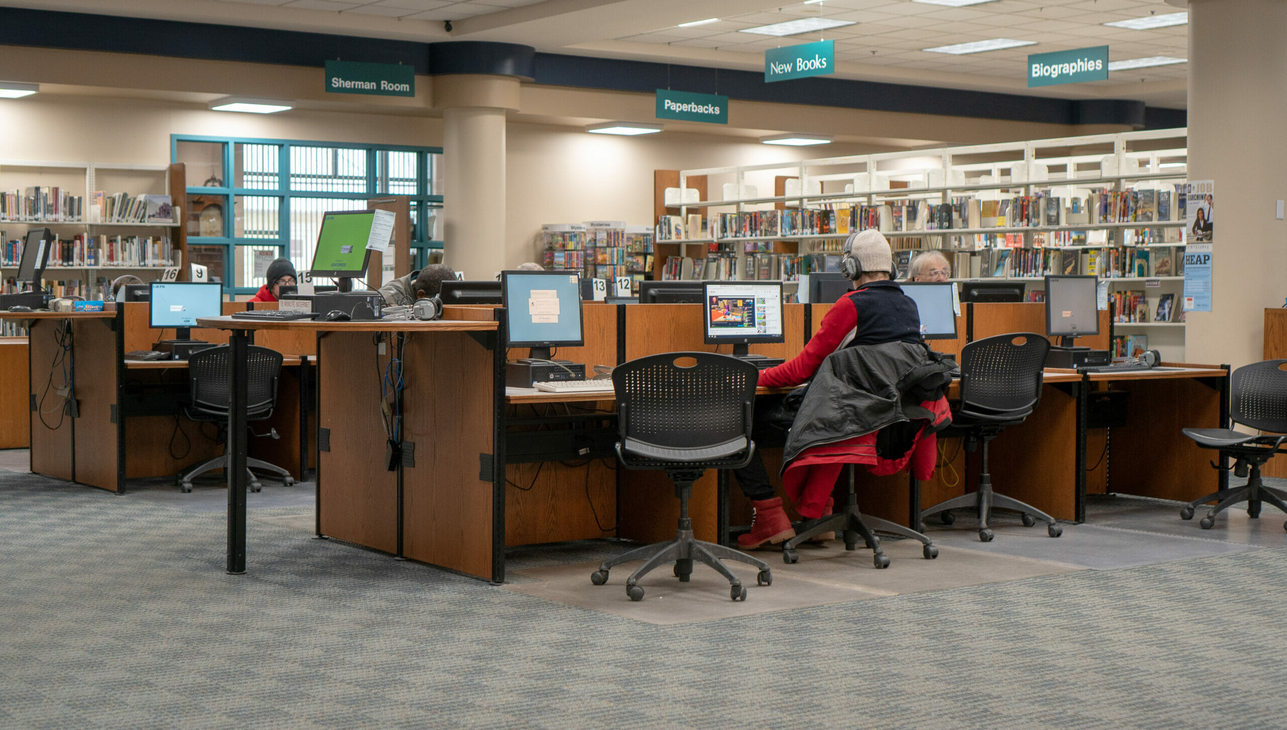 Several adults use public computers seated at desks in the Main Library Reference department.