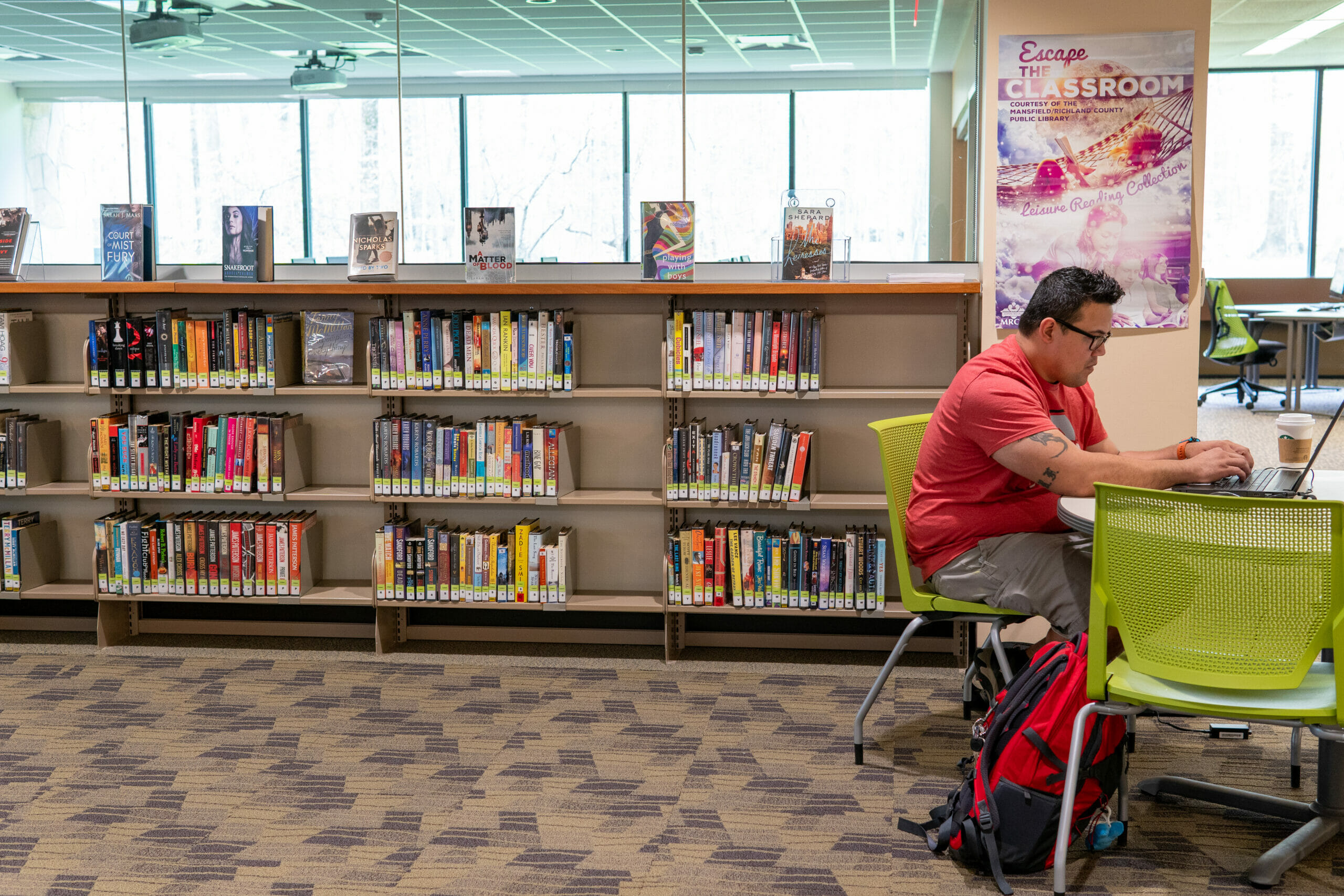 A person works on a laptop seated at a table near bookshelves in a the Bromfield Library at OSU-Mansfield.