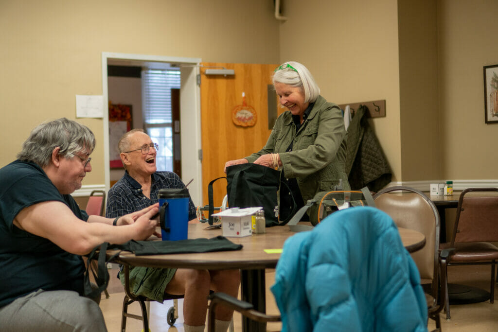 An outreach department staff member laughs with a customer at a care facility while delivering library materials.