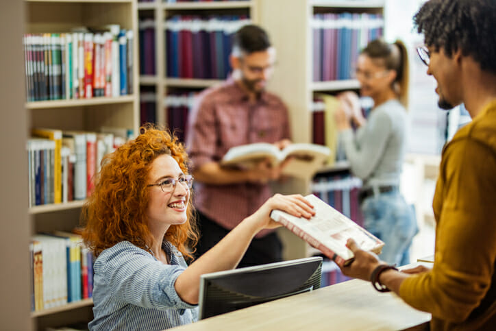 Happy librarian taking a book from a student in the library.
