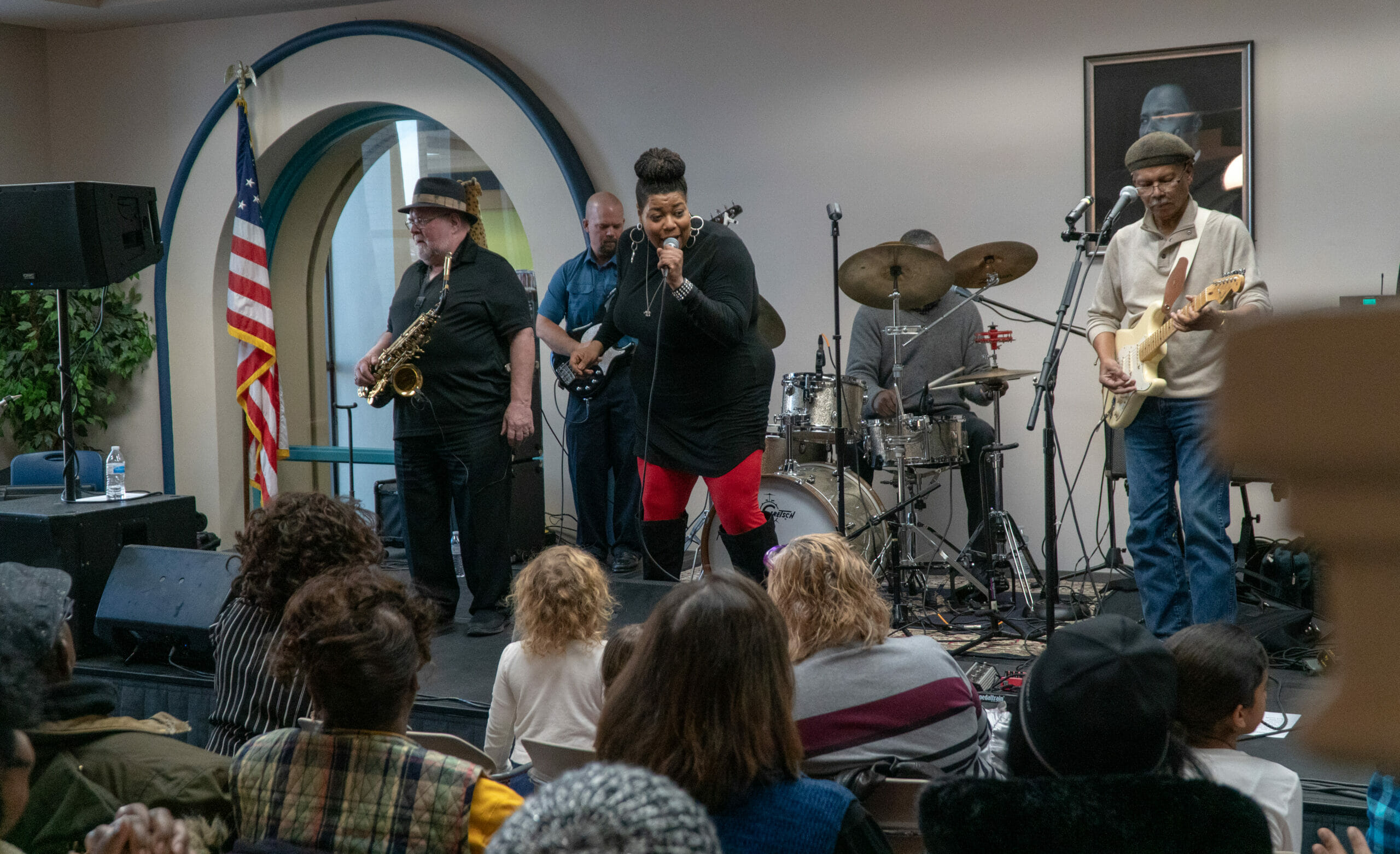 A woman sings in a 5 person band on a stage in the 2nd floor lobby at the Main Library