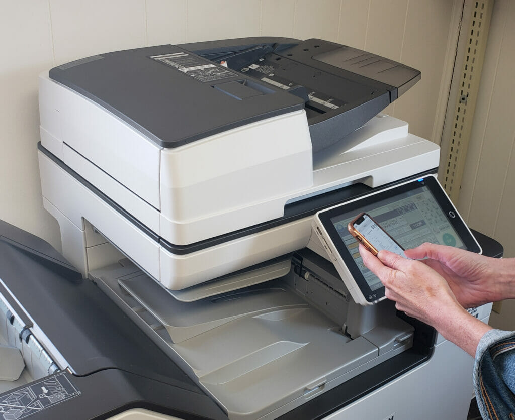 Hands a a person using a mobile phone to remotely print a document at a printer at the Library