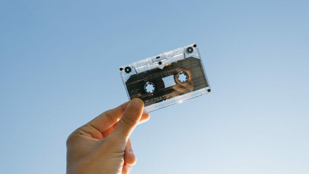 A hand holds a cassette tape up to the sky.
