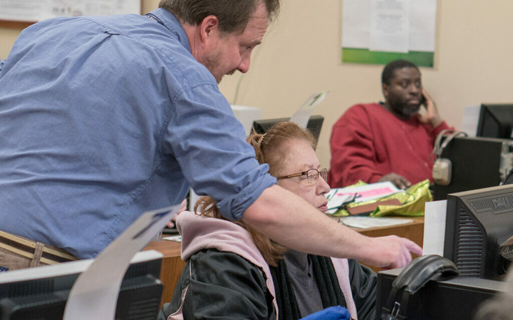 Staff member in the Learning Lab at the Main Library assists a person while pointing to a computer screen in a classroom setting.