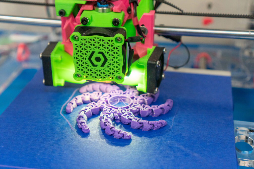 closeup of a green and pink 3D printer printing a purple octopus