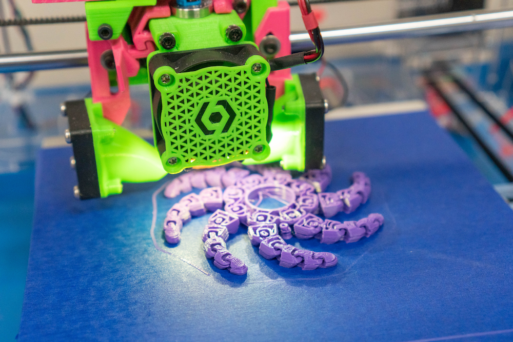 closeup of a green and pink 3D printer printing a purple octopus