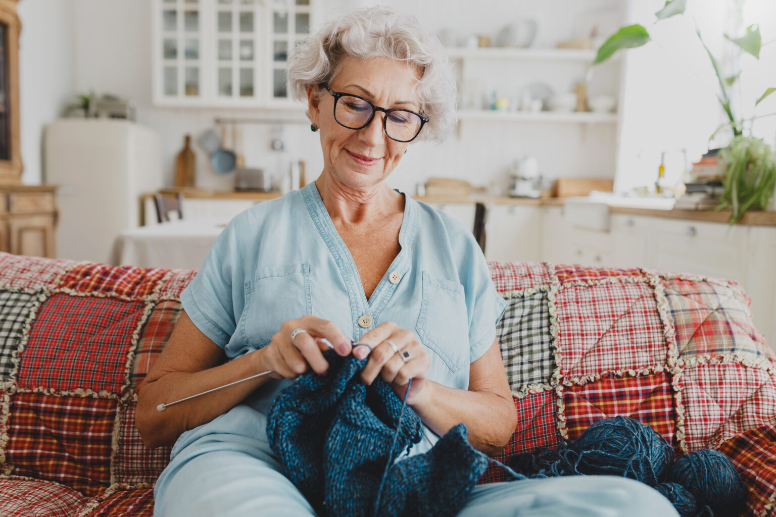 Lovely grandmother knitting cardigan sitting on the sofa in glasses.