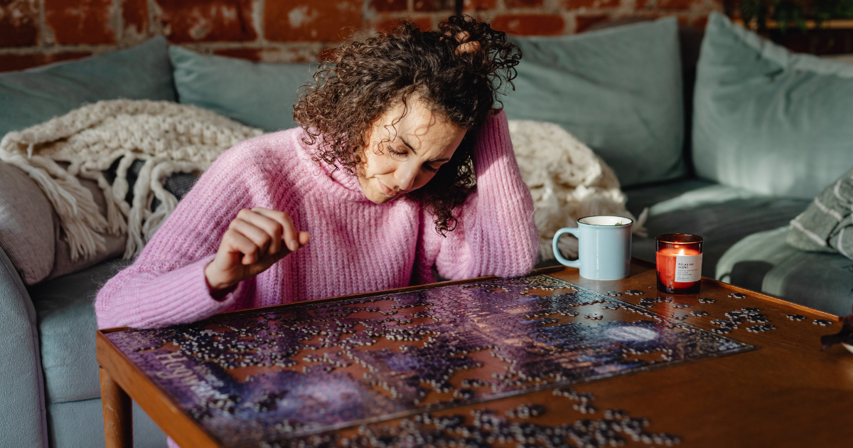 A person working on a puzzle on a table with a mug and candle