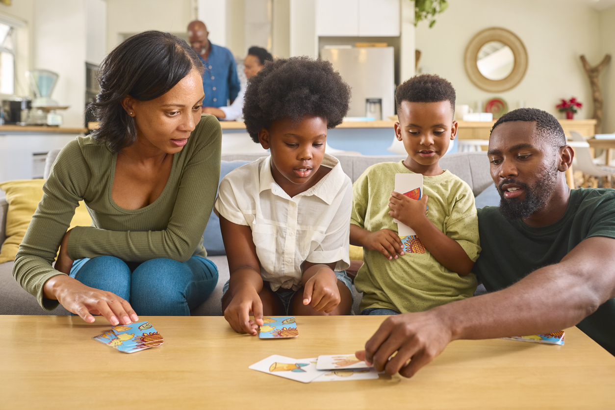 Family Indoors At Home With Playing Cards With Grandparents In Background