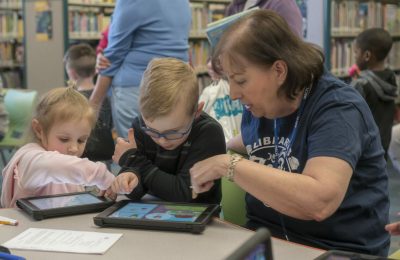 Person helping young children with a learning app on a tablet
