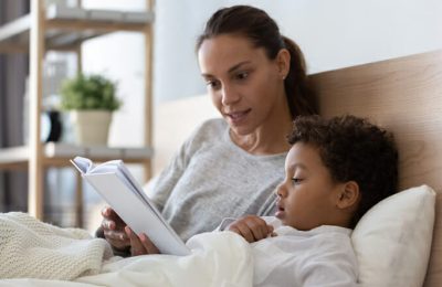 Loving young mom lying in bed with little child reading a story.